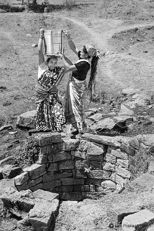 Struggling to balance a larger drum of water filled from the open well in Gumla district shown earlier in Jharkhand, India